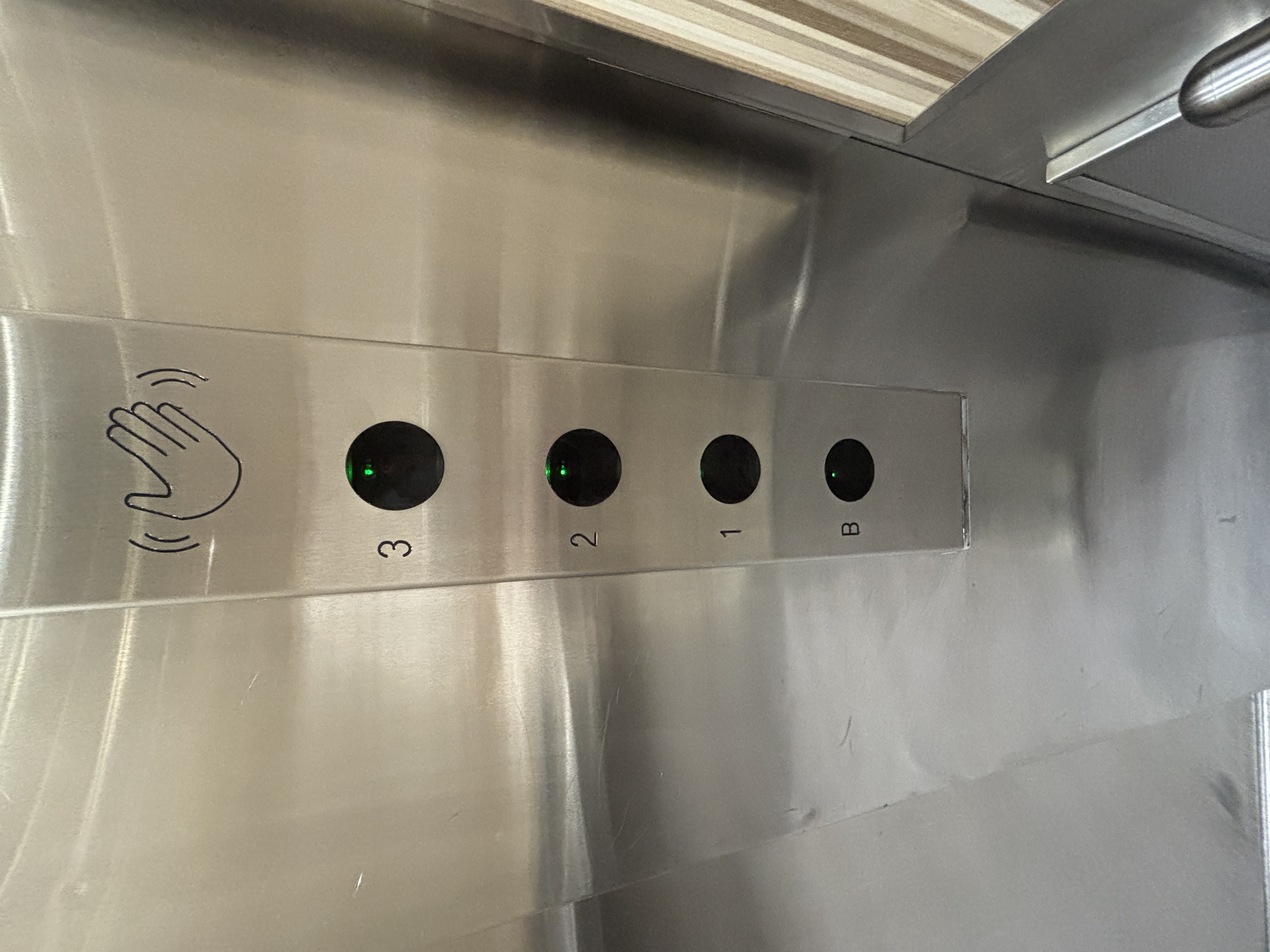 Touchless elevator button that emits an electronic chime when a hand waves over it.