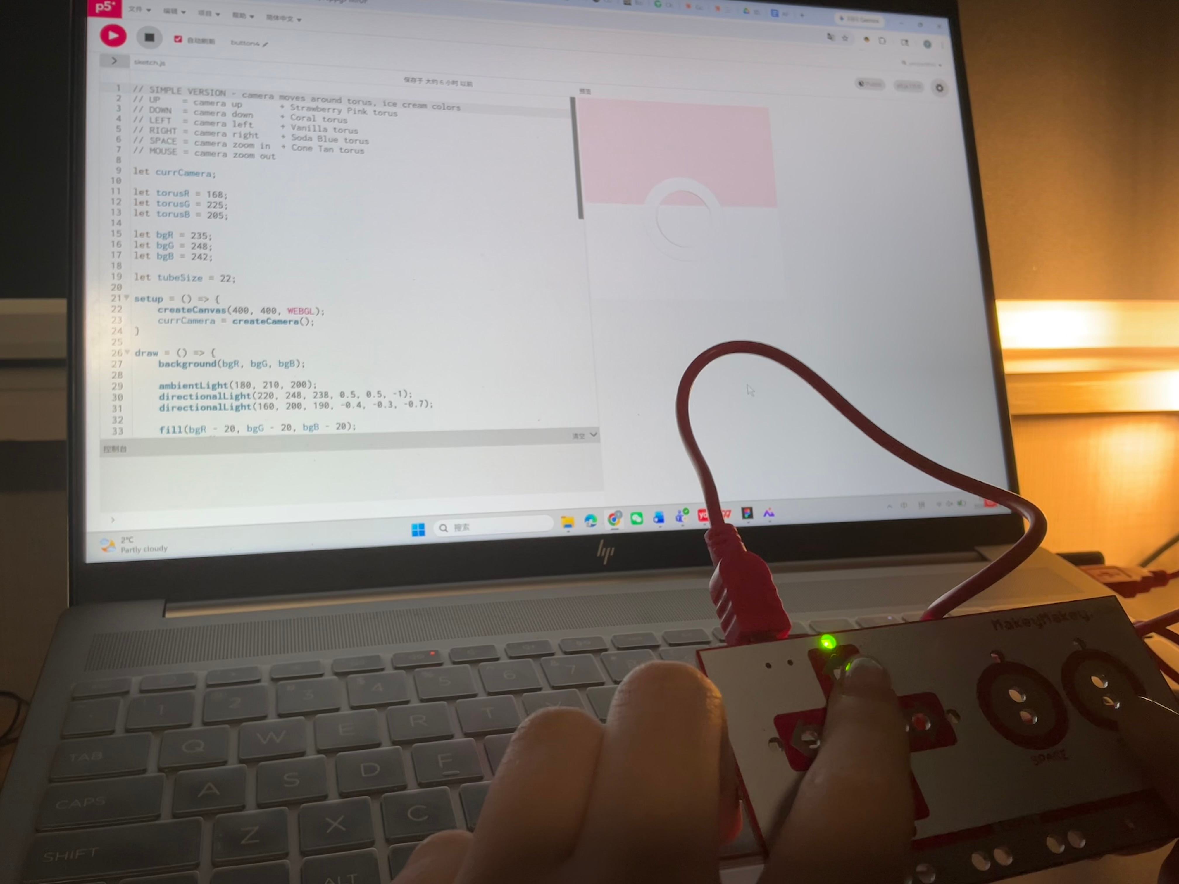 Laptop shows a pale torus with ribbon confetti flying outward, Makey Makey resting beside it.