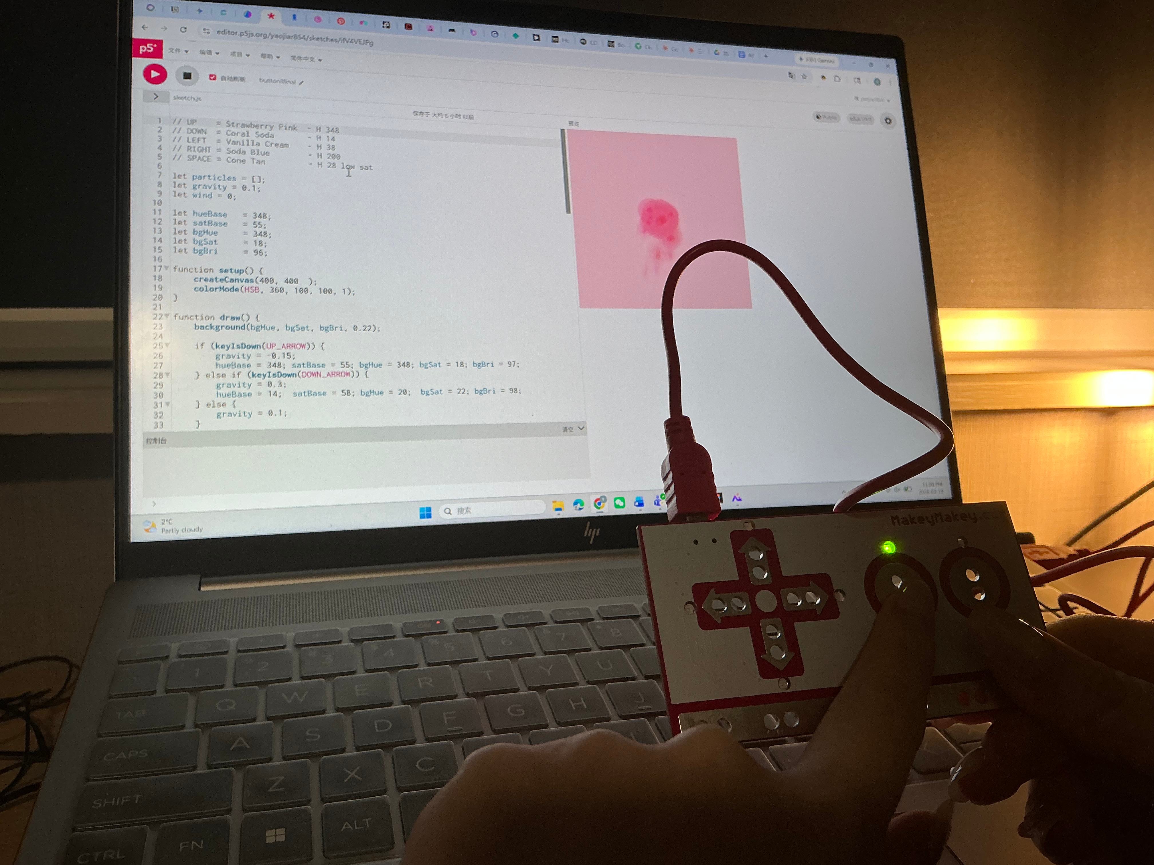 Laptop screen shows code on the left and a pink circle on a blue canvas on the right, Makey Makey arrows pointed up.