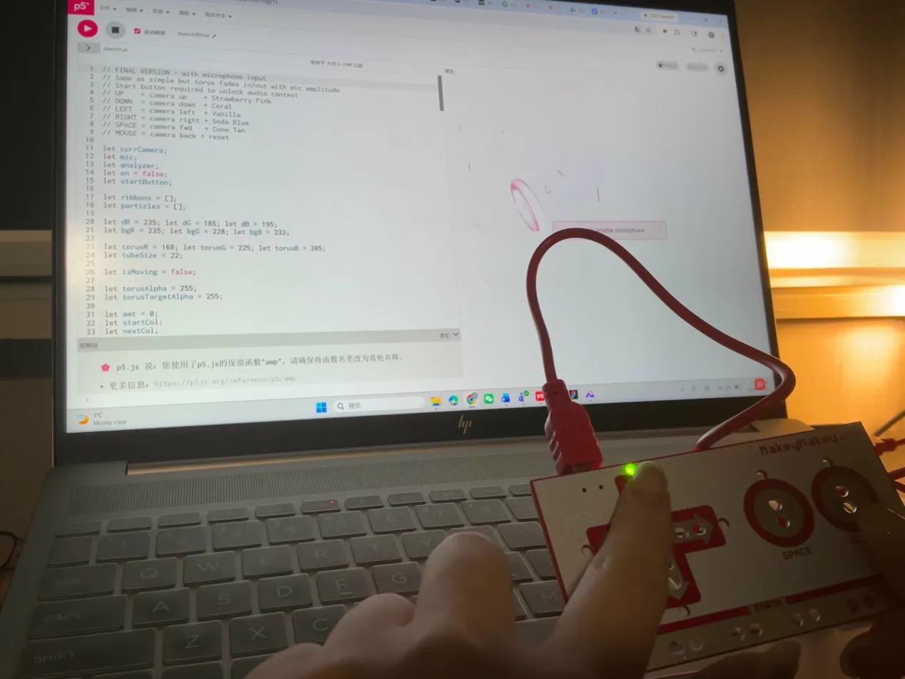 Laptop shows a pink torus surrounded by scattered ribbon confetti, Makey Makey connected via red cable.