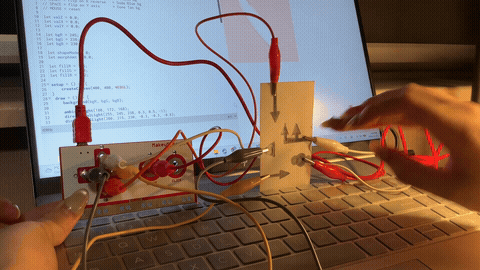 The image displays a hand touching the pencil-drawn graphite arrow buttons triggering a shifting visual on the laptop screen, using pencil graphite as the conductive input material.