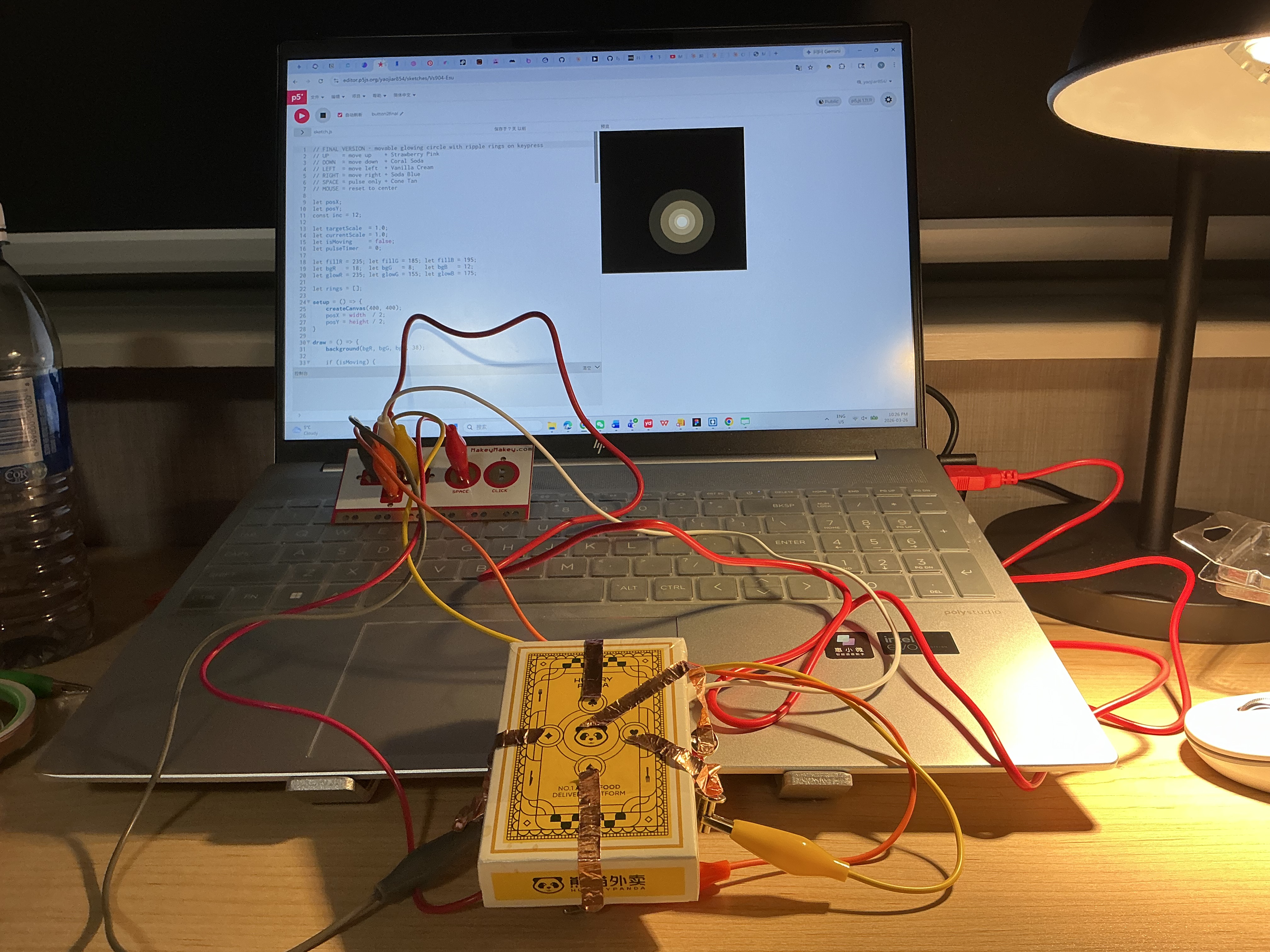 The image displays a laptop screen showing a dark canvas with a small glowing amber dot while the yellow copper tape box sits connected below, confirming the copper tape interface is triggering the glow sketch.