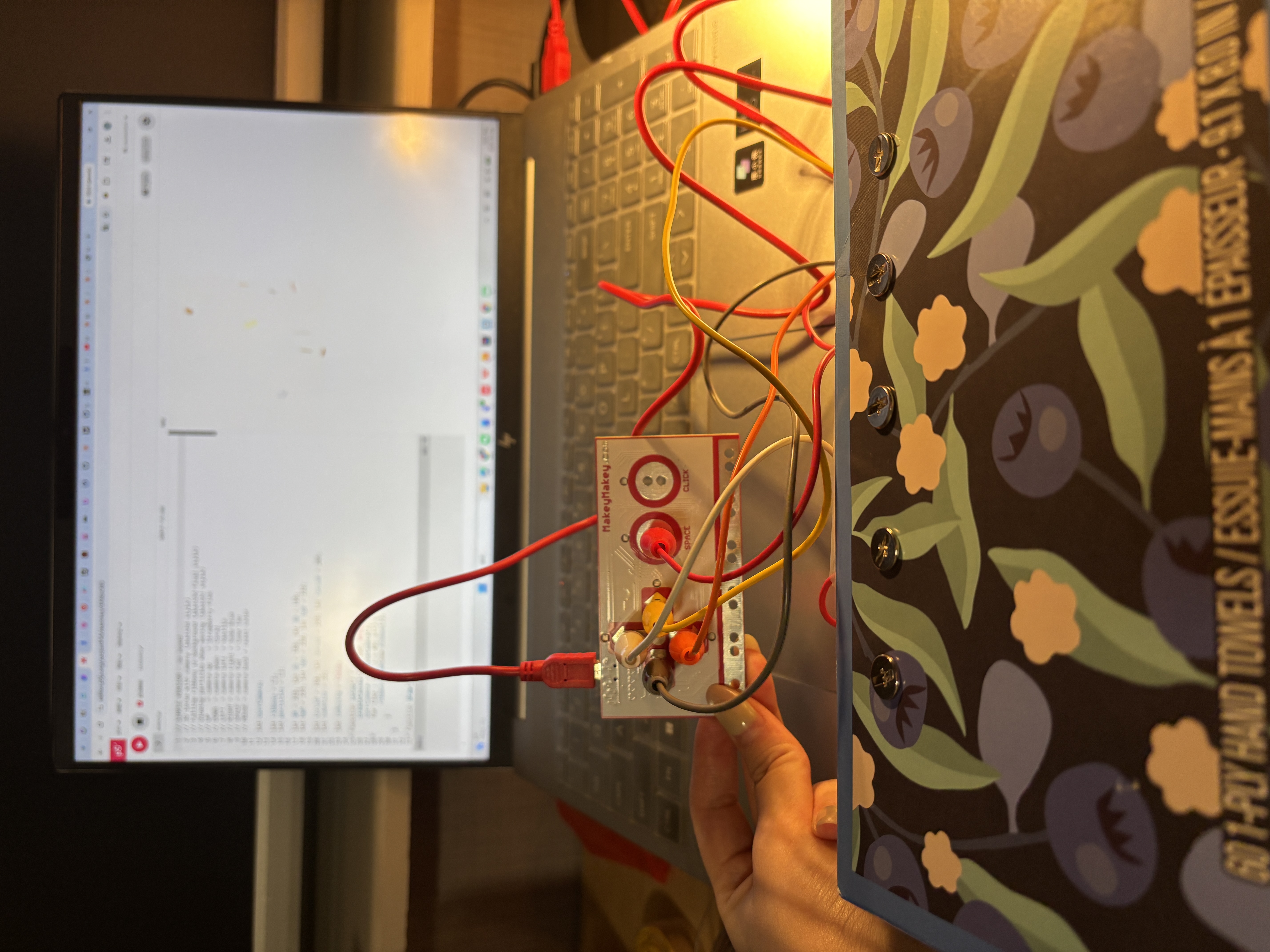 The image displays a laptop showing a blank white canvas while the Makey Makey sits beside it with wires spread across the keyboard, testing the initial circuit connection before interaction.