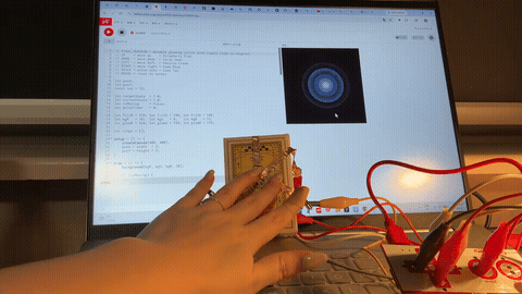 The image displays a hand pressing the copper tape strips on the yellow box and triggering a glowing dot that shifts color on the dark laptop screen, using copper tape as the five-button conductive interface.